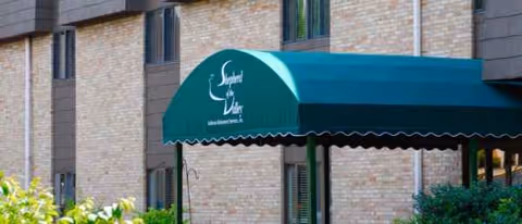 Brick senior living facility entrance with green canopy reading Shepherd of the Valley.