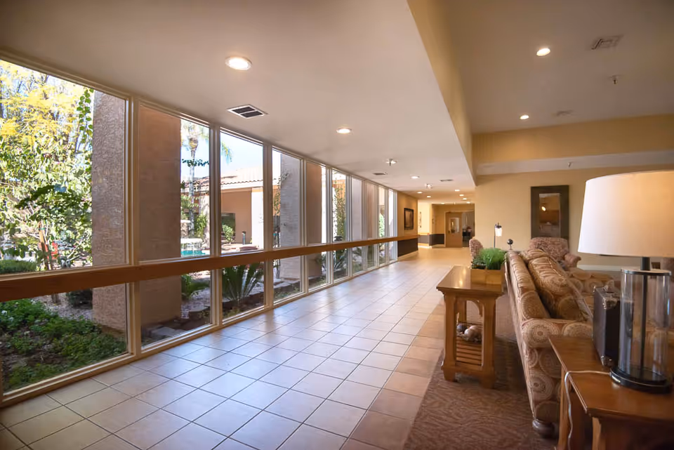 Sunny interior hallway with floor-to-ceiling windows and a seating area with couches and side tables.
