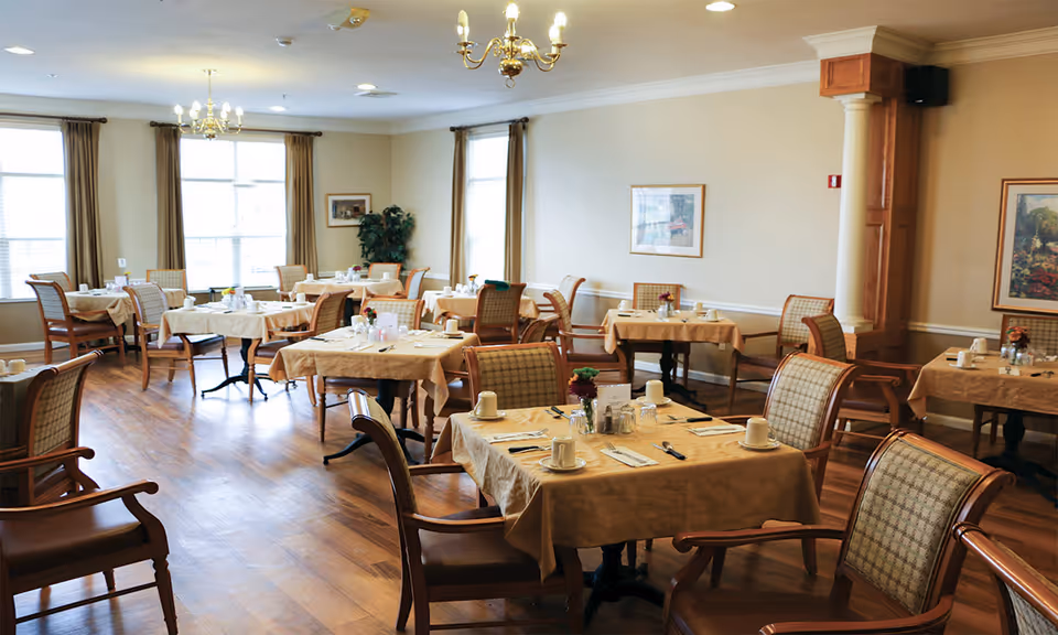 Bright dining room with multiple set tables and chairs arranged on a hardwood floor.