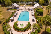 Aerial view of a rectangular outdoor swimming pool with an adjacent circular hot tub, lounge chairs, palm trees, and two poolside structures.