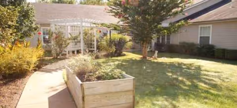 Sunny exterior courtyard with walkway, raised planters, and a lawn in front of a residential building.