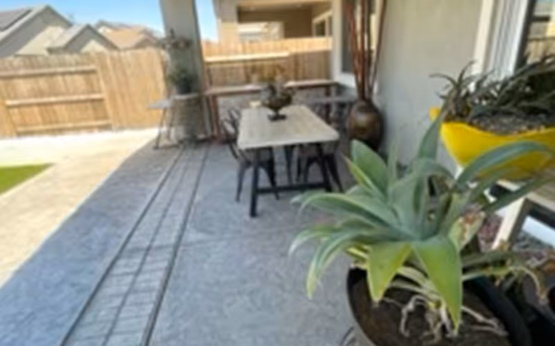 Covered patio with a table and chairs, potted plants, and a fenced backyard.