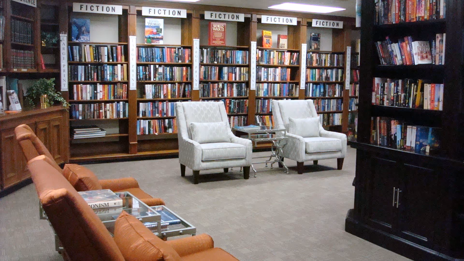 Library-style common room with bookshelves labeled 'FICTION' and several armchairs and seating.