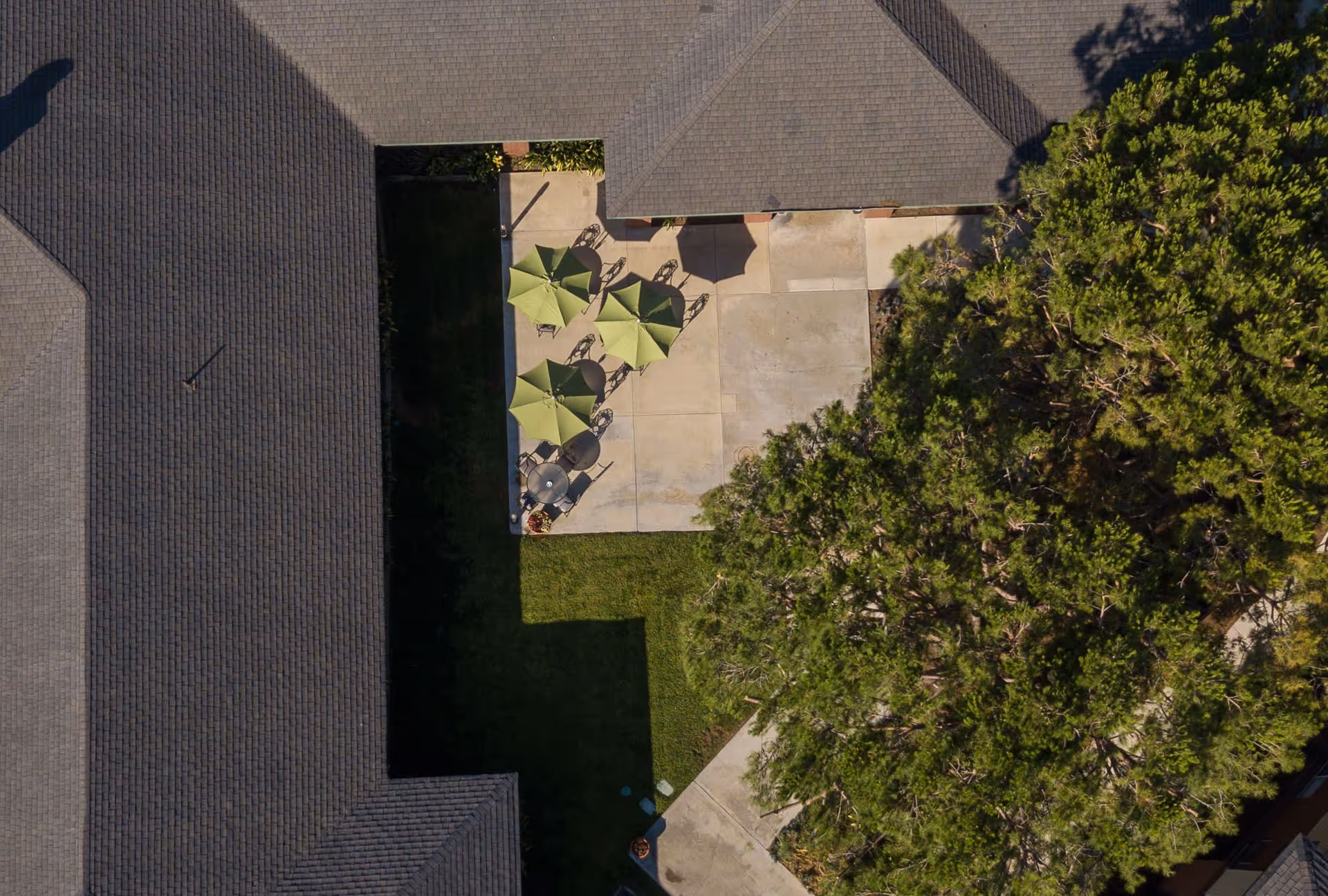 Aerial view of an outdoor patio area at Carmel Village Retirement Community with several green umbrellas shading tables and chairs, surrounded by building rooftops and a large tree.