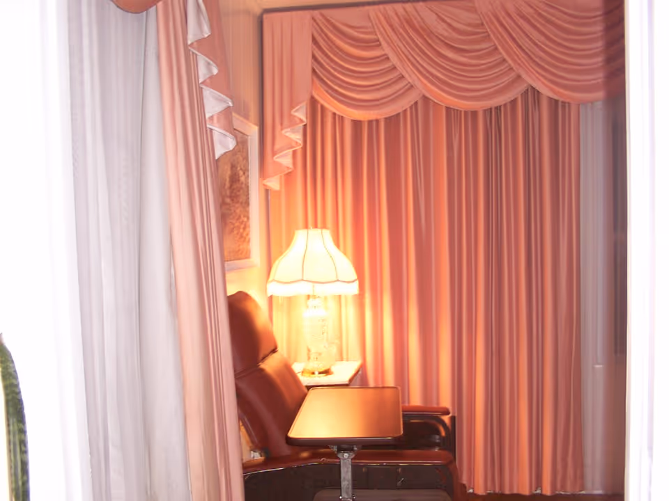 A cozy seating nook with a leather recliner, a side table and lamp, framed by pink draped curtains.