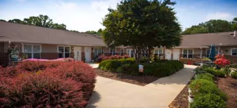 Single-story Brookdale Monroe Square exterior with a central walkway, trees, and landscaped shrubs.