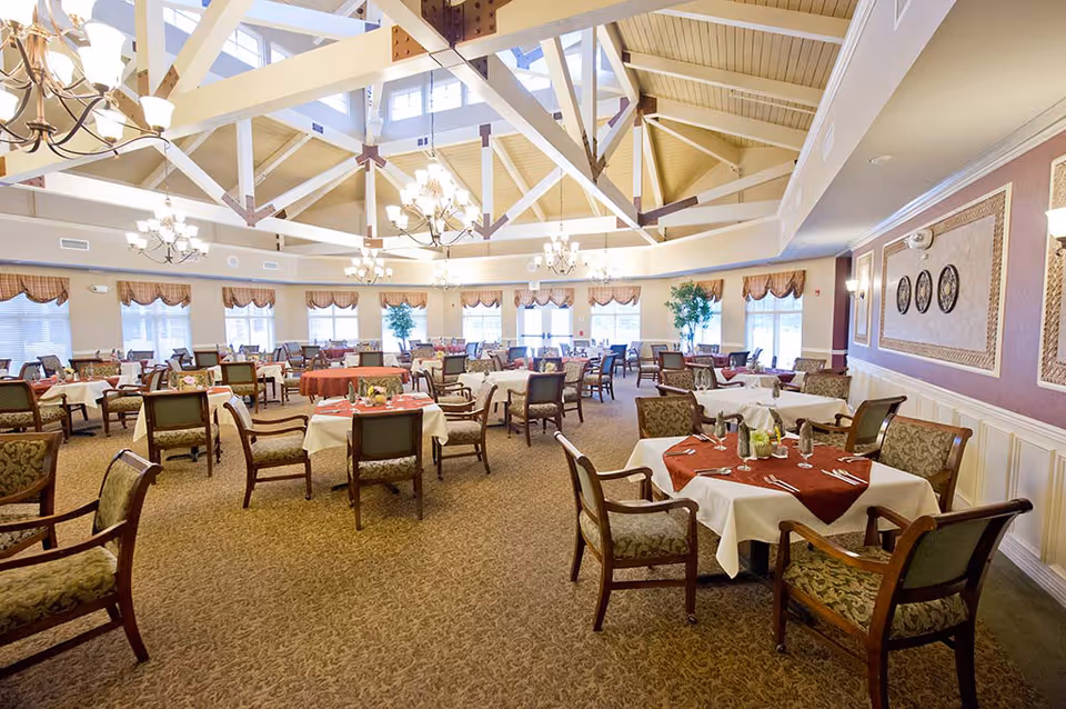 Spacious dining room with multiple tables set with white tablecloths under a high beamed ceiling and chandeliers.