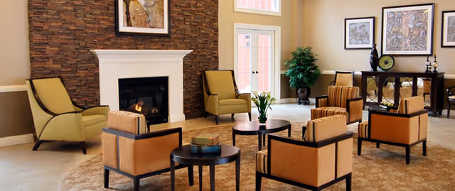 Sunlit communal living room with a stone fireplace, arranged armchairs and small coffee tables.