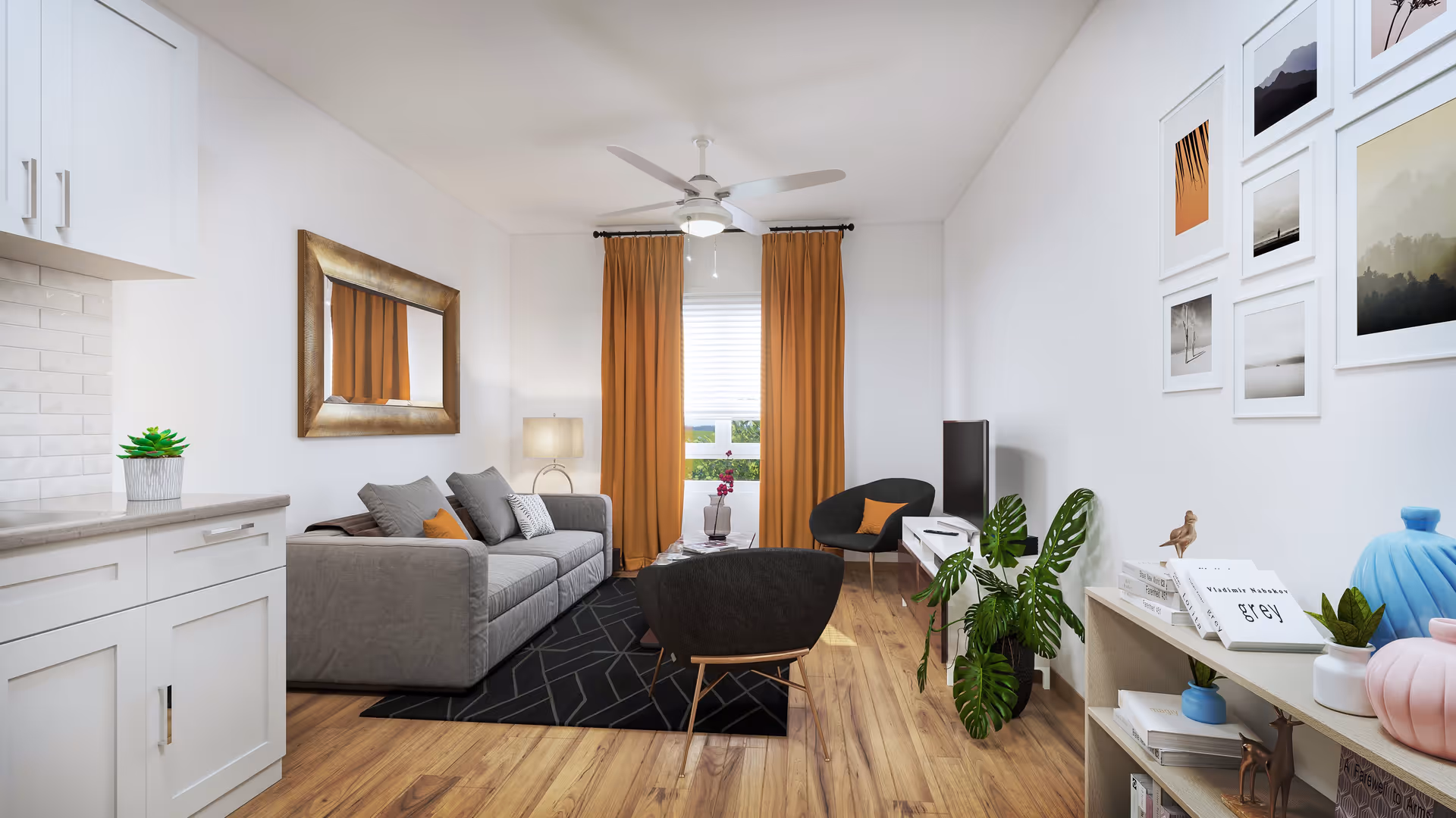 A modern living room with a gray sofa, two black chairs with orange cushions, a black geometric rug, and a ceiling fan with light. The room has wooden flooring, white walls decorated with framed pictures, and orange curtains covering a window. There is a white TV stand with a flat-screen TV, a wooden shelf with books and decorative items, and a small potted plant on the floor.