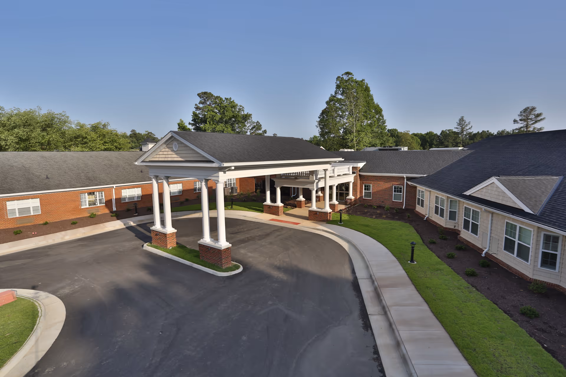 Covered front entrance and porte-cochere with white columns and a curved driveway at a brick senior living building.