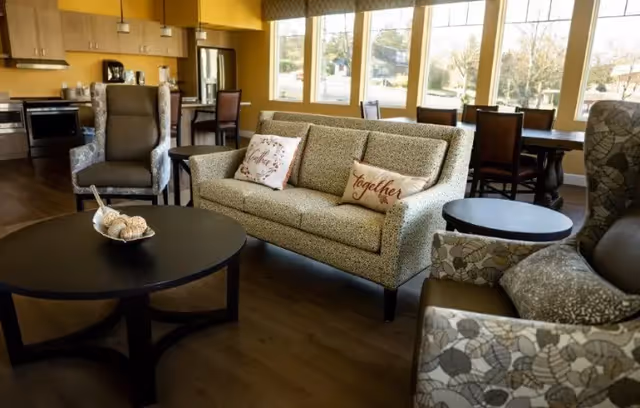 Communal living area with a sofa, armchairs, coffee table, dining table and a kitchenette in the background.