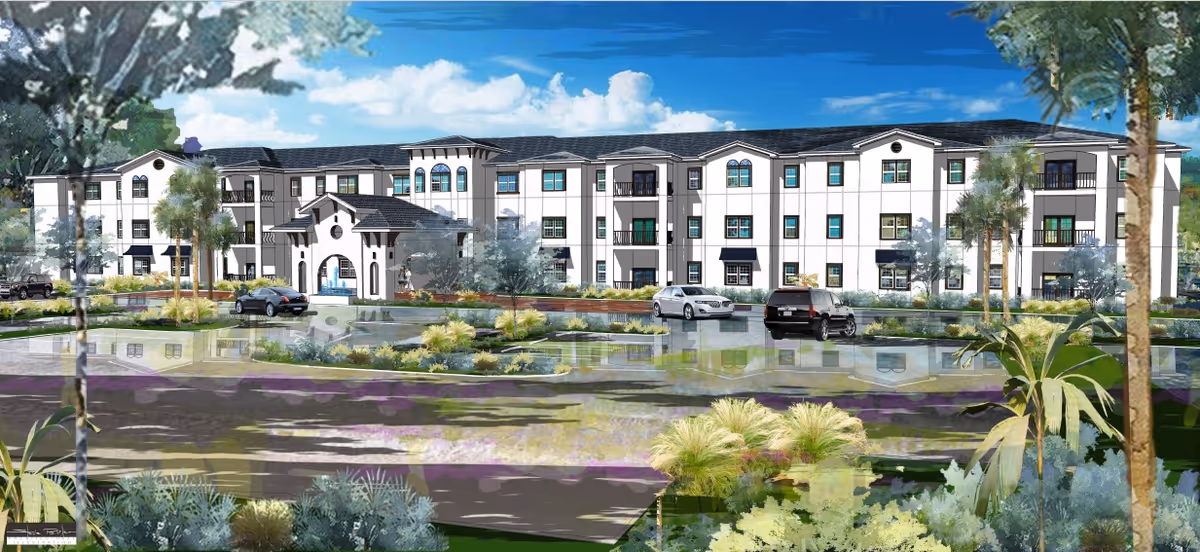 Exterior view of a large, three-story senior living facility building with a central entrance, surrounded by landscaped greenery and a parking area with several cars parked. The sky is blue with some clouds.