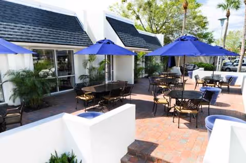 Outdoor patio with blue umbrellas and metal tables outside a white building.