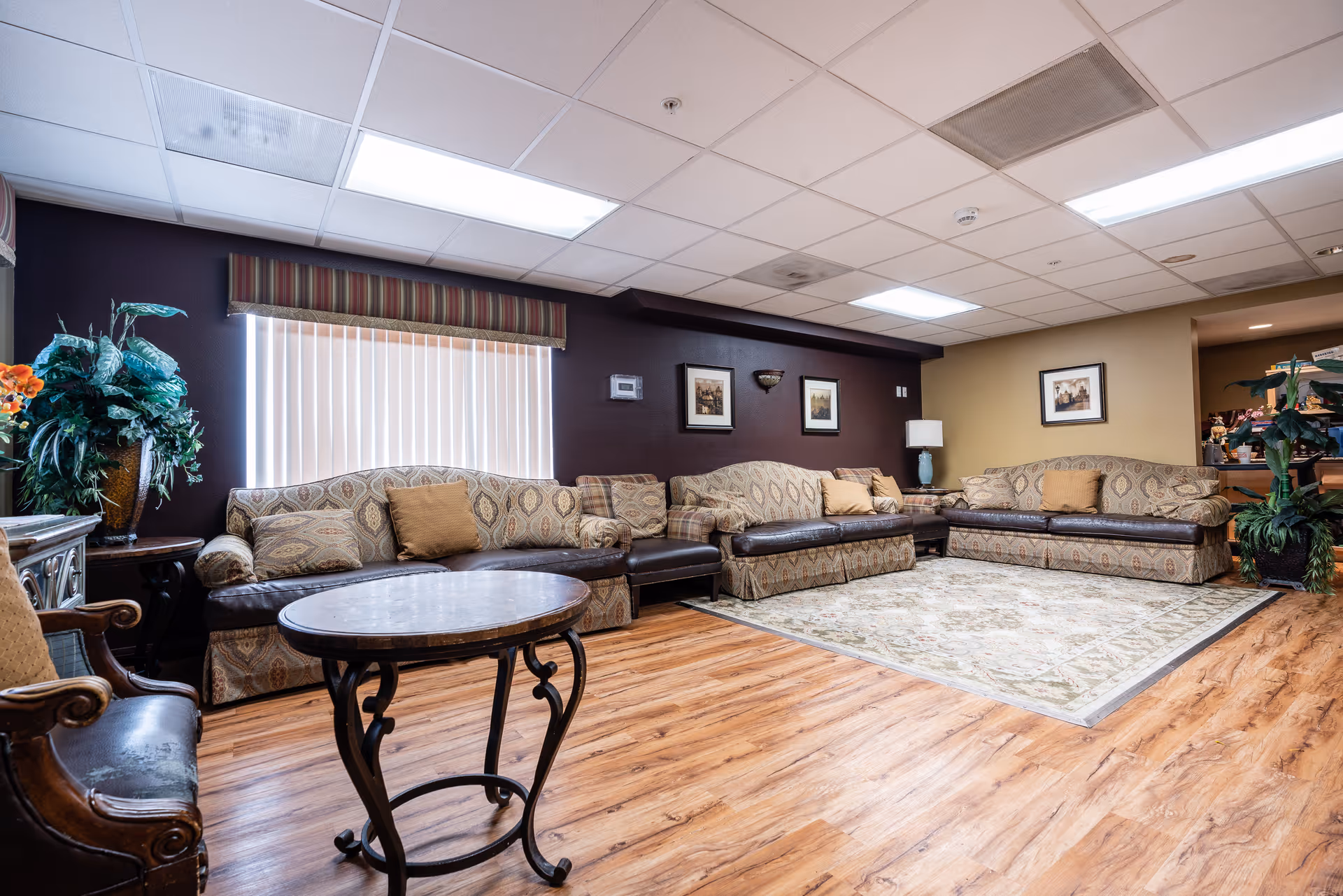 Comfortable lounge with patterned sofas arranged around an area rug, a round coffee table, potted plants and framed wall art.