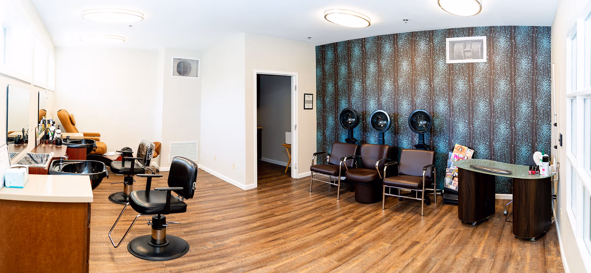 Bright salon room with styling chairs, hooded hair dryers, a manicure station and a patterned accent wall.