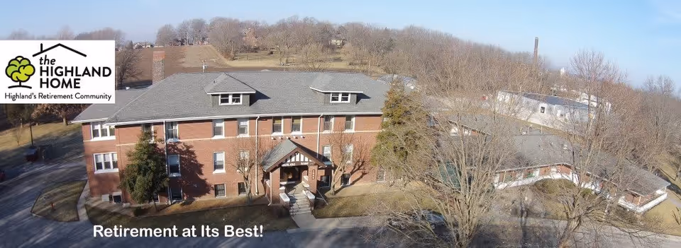 Aerial view of a large brick retirement home building surrounded by leafless trees and open land under a clear sky. The building has multiple windows and a main entrance with a small porch. The Highland Home logo is visible in the top left corner with the text 'Highland's Retirement Community' and 'Retirement at Its Best!' is written at the bottom.