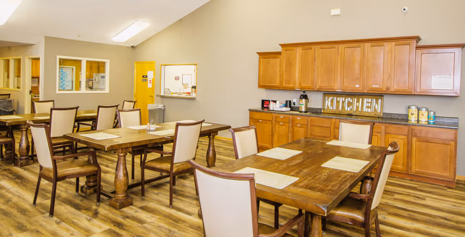 Dining room with wooden tables and chairs and a kitchenette with upper cabinets and a sign reading 'KITCHEN'.