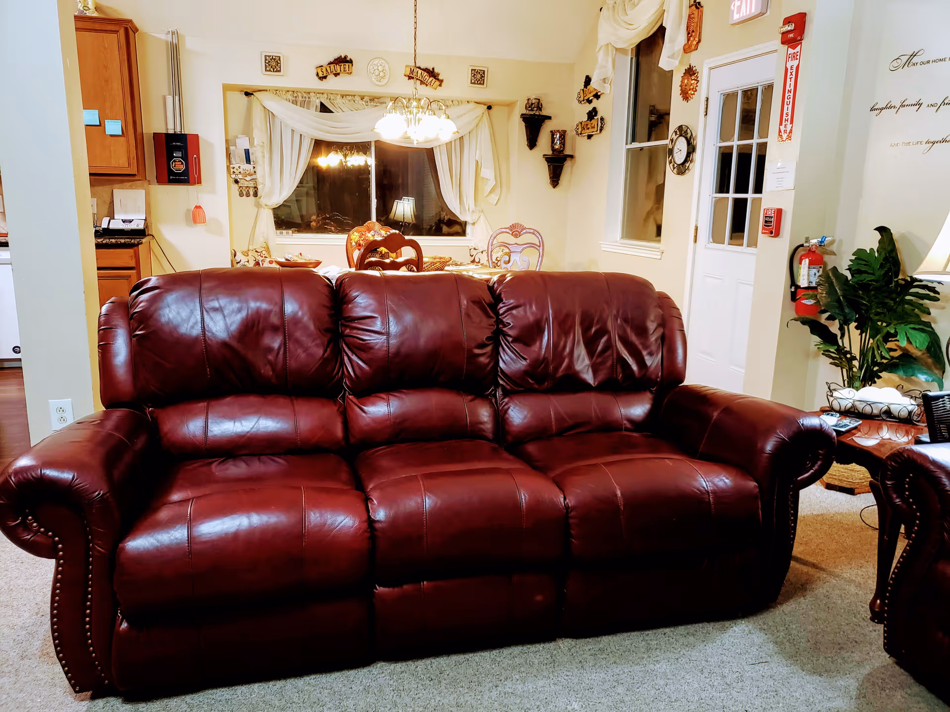 A burgundy leather three-seat sofa in a cozy living room with a dining area visible in the background.