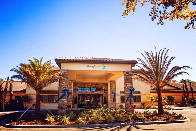 Front entrance of Inspired Living Sarasota senior living facility with palm trees, landscaping, and a covered porte-cochère.
