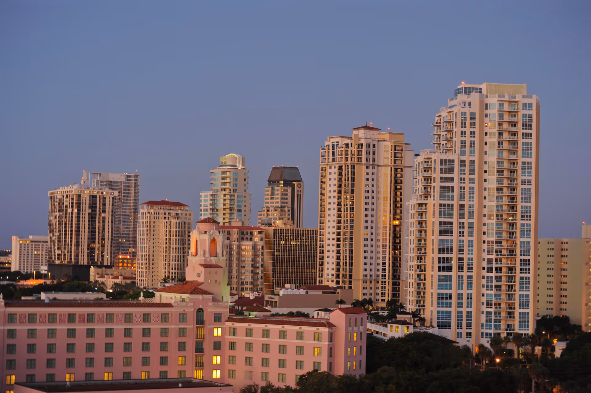Dusk view of a city skyline with multiple high-rise residential towers and a pink hotel building in the foreground.