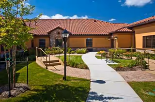 Sunlit exterior of a San Remo senior living facility with a curved walkway and entrance.