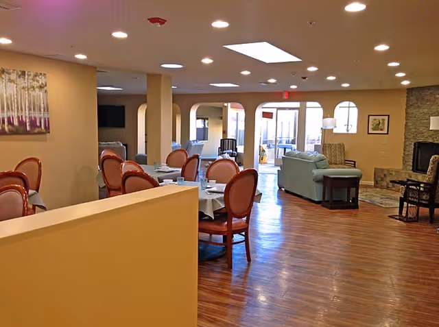 Open communal dining and lounge area with round dining tables and upholstered chairs, sofas, a fireplace and wood floors.