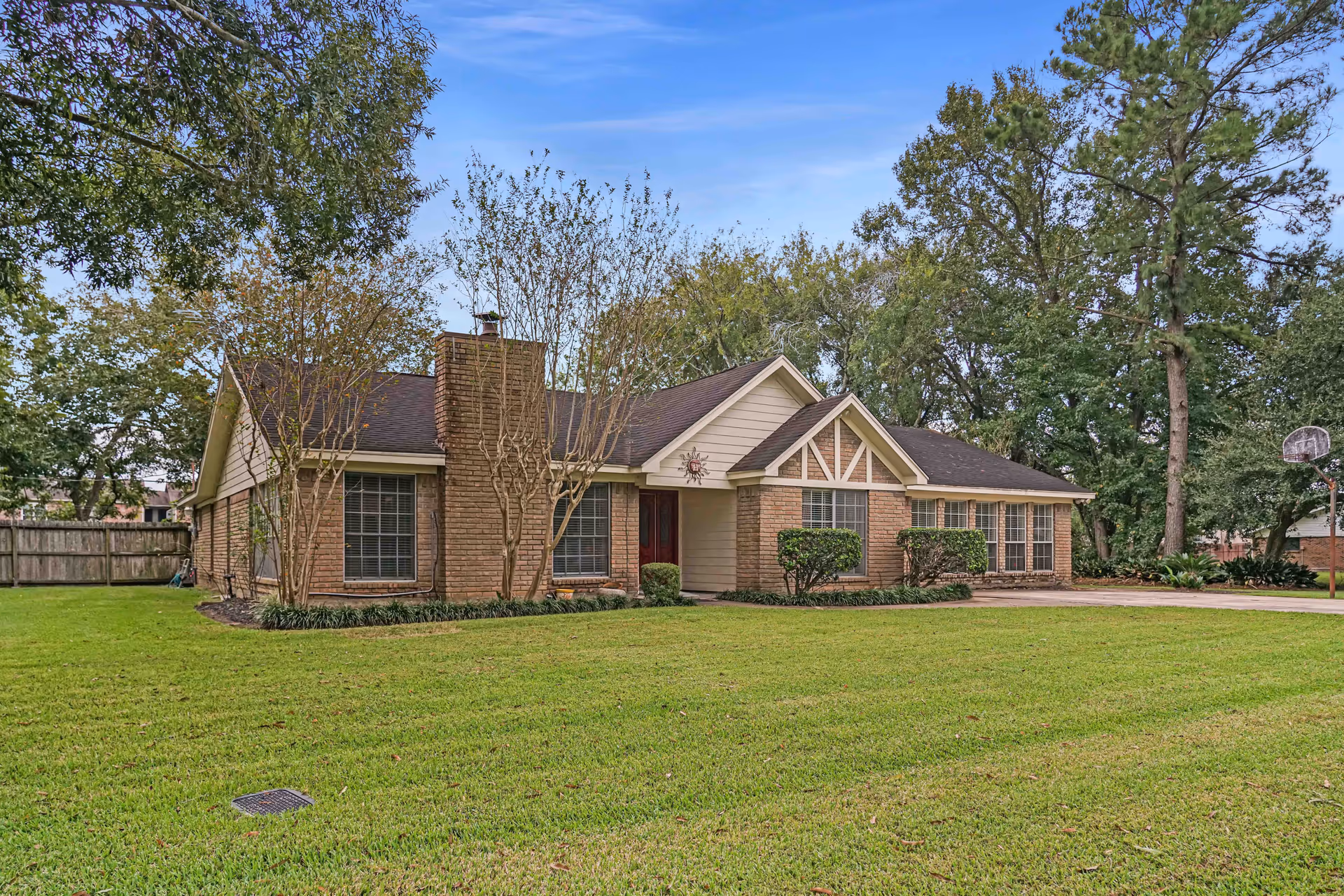Single-story brick house with a dark roof surrounded by a large, well-maintained green lawn and several trees under a clear blue sky.