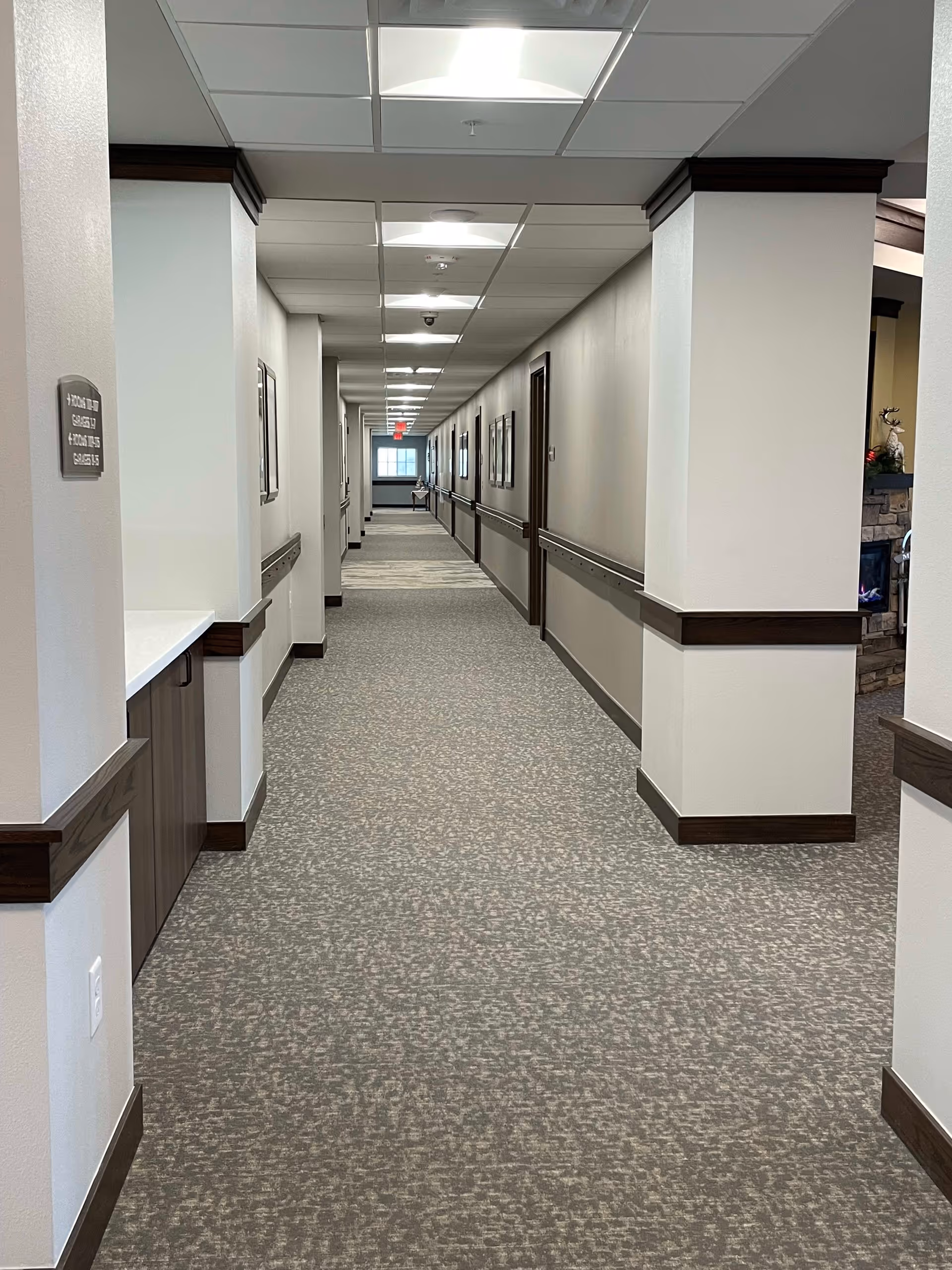 Long carpeted interior hallway in a senior living facility with handrails and doors along both sides.