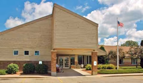 Exterior view of Wellington Meadows senior living facility with a covered entrance and flagpole.