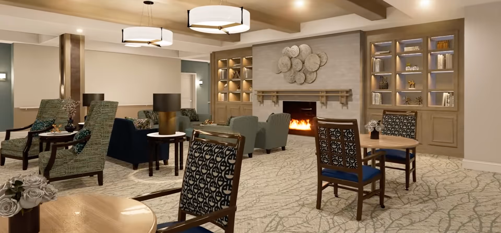 Cozy senior living common room with chairs and small tables arranged around a lit fireplace and built-in bookshelves.