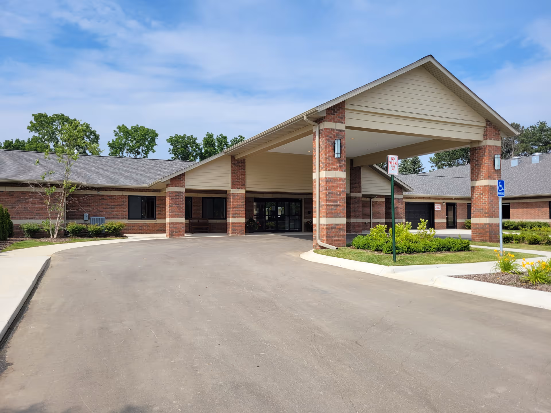 Front entrance of a single-story brick assisted living building with a covered porte-cochère and landscaped driveway.