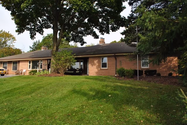 Single-story brick building with a green lawn and large trees in front.