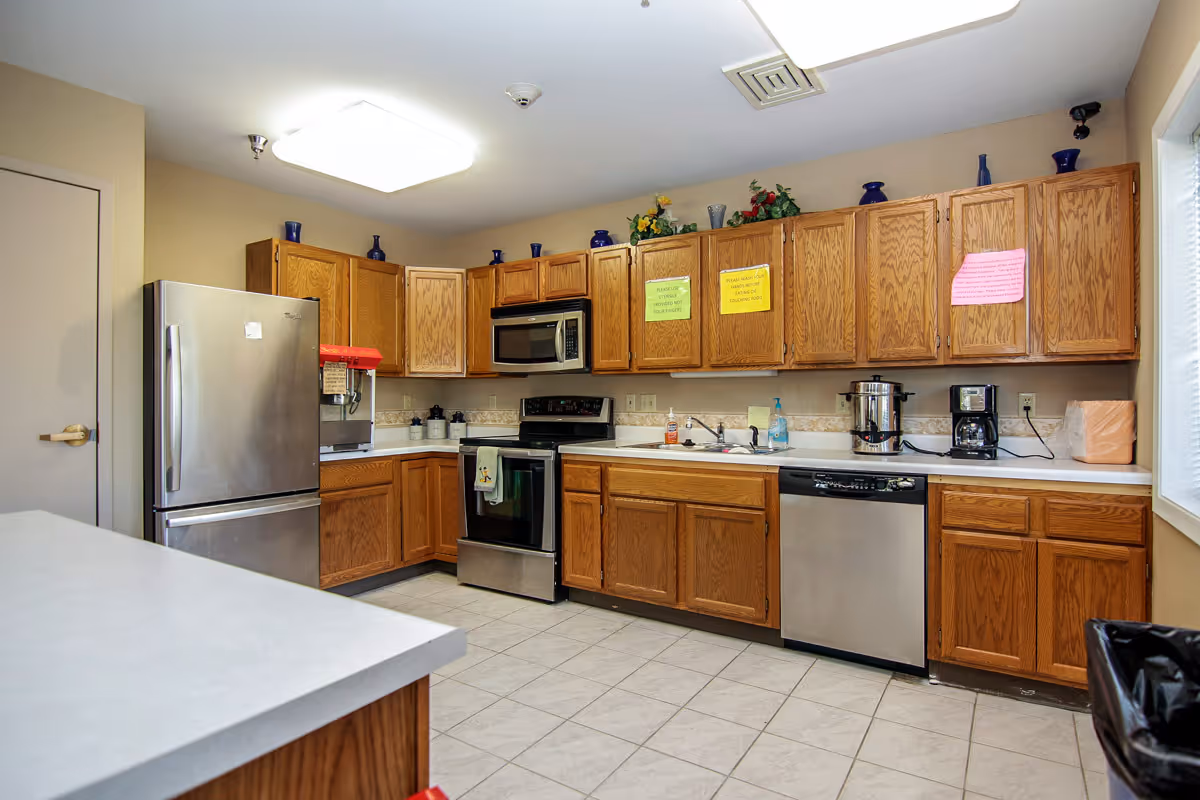 Well-lit communal kitchen with oak cabinets, stainless steel refrigerator, stove, dishwasher, microwave, and countertops.