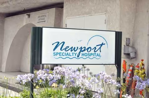 Exterior view of Newport Specialty Hospital sign with blooming flowers in front.