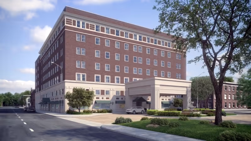 Front exterior of a multi-story brick senior living building with a covered porte-cochere, driveway, and landscaped grounds.
