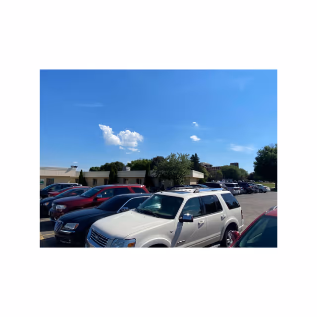 Parking lot with multiple parked cars in front of a single-story building under a blue sky.