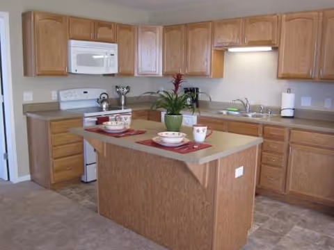 Wooden kitchen with island, ample cabinets, stove, microwave, and sink.