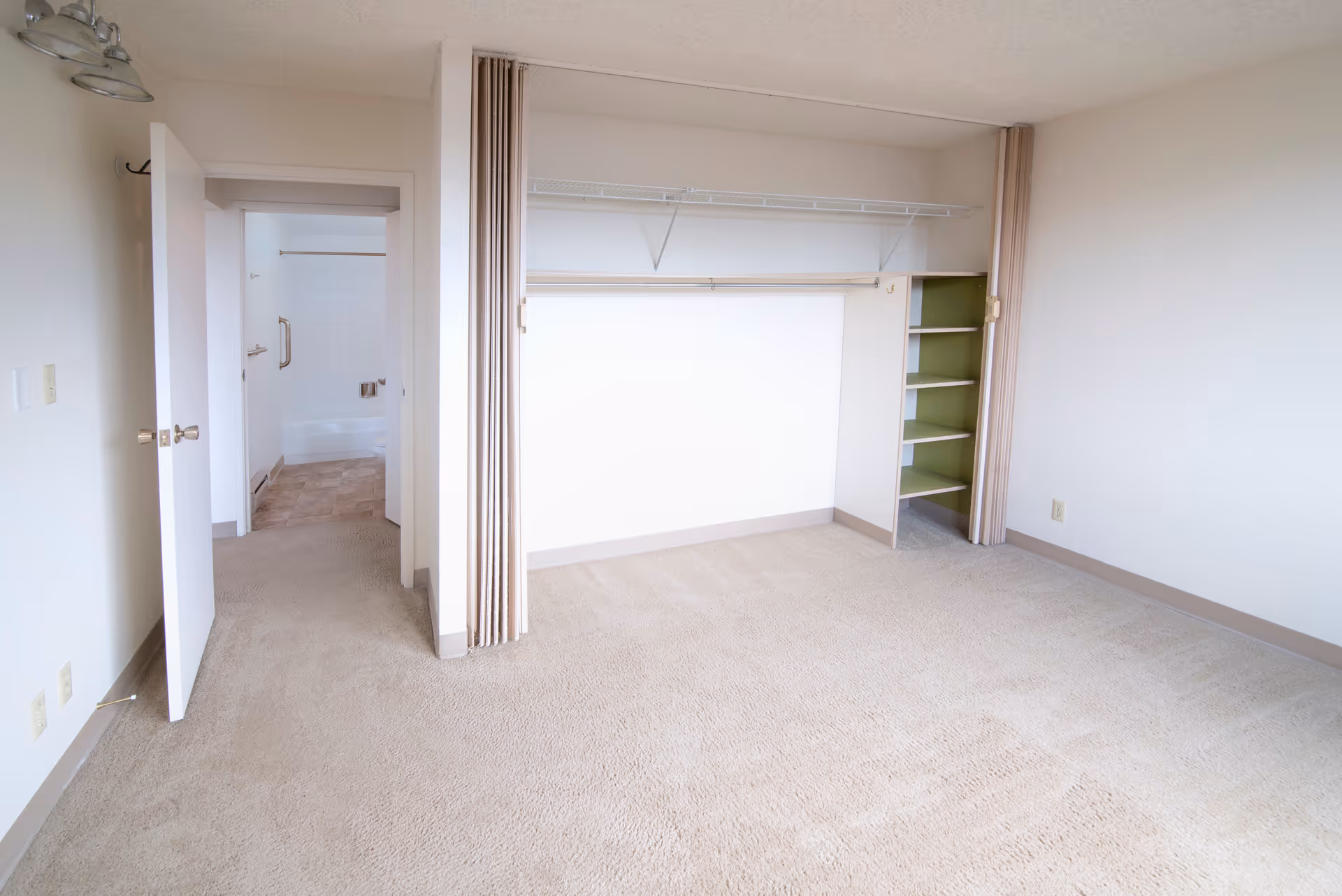 Empty carpeted bedroom with an open closet and a doorway leading to a bathroom.