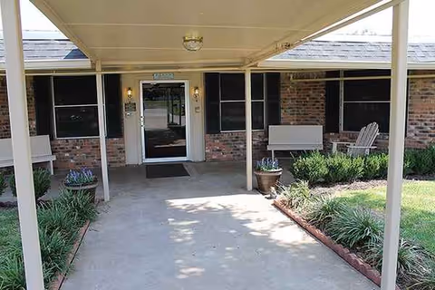 Covered entrance to Teague Nursing and Rehabilitation, brick building with benches and potted plants.