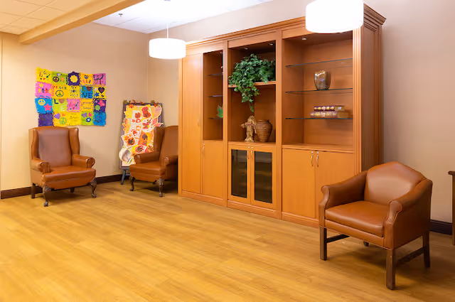 A bright common room with three leather armchairs, a wooden display cabinet, hanging lights and colorful wall art.