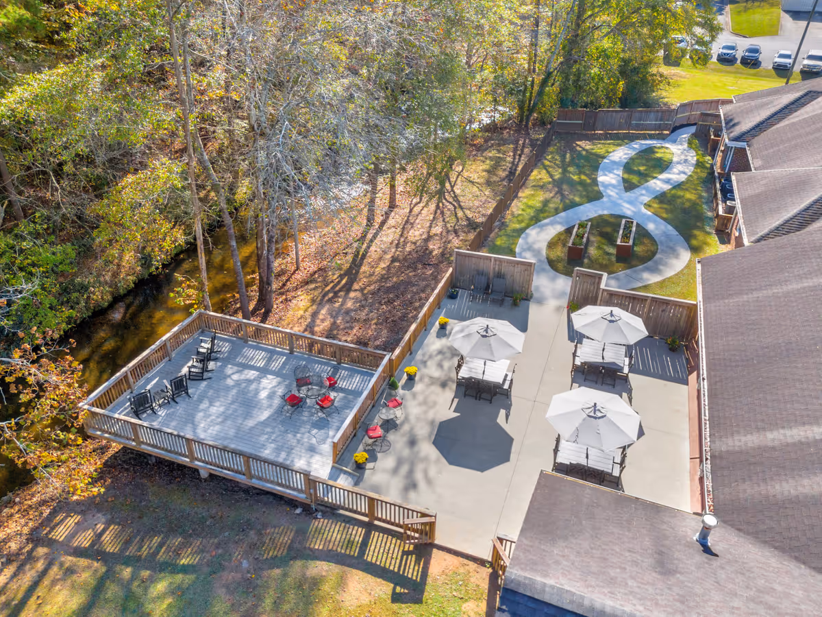 Aerial view of an outdoor patio area at Overlook Toccoa featuring multiple seating arrangements with umbrellas, a wooden deck with chairs, a winding concrete path, and surrounding trees and greenery.