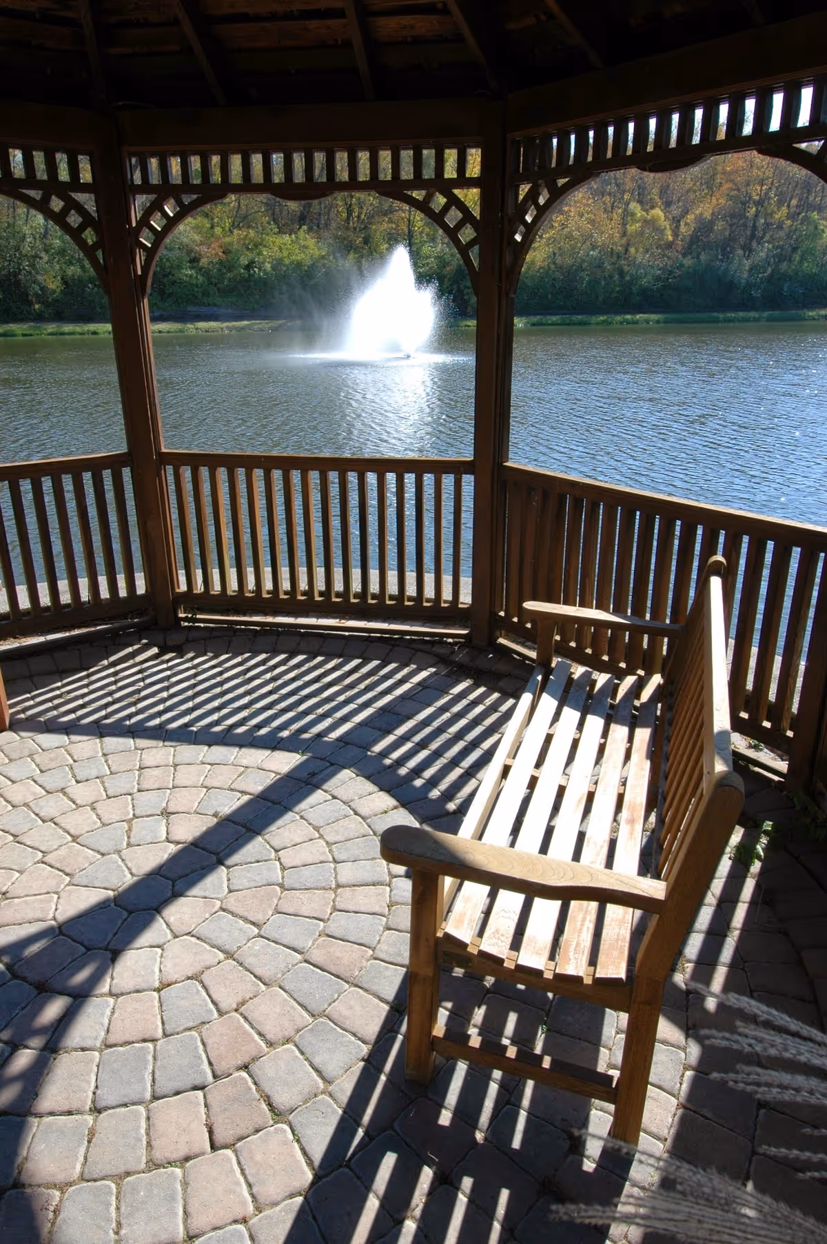 Wooden gazebo with a bench overlooking a pond with a fountain in the center.