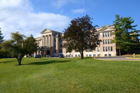 Stone building with imposing columns, green lawn, and several trees under a blue sky