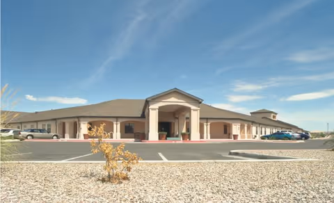 Wide exterior view of a single-story building with a covered entrance and a parking lot in front under a clear blue sky.