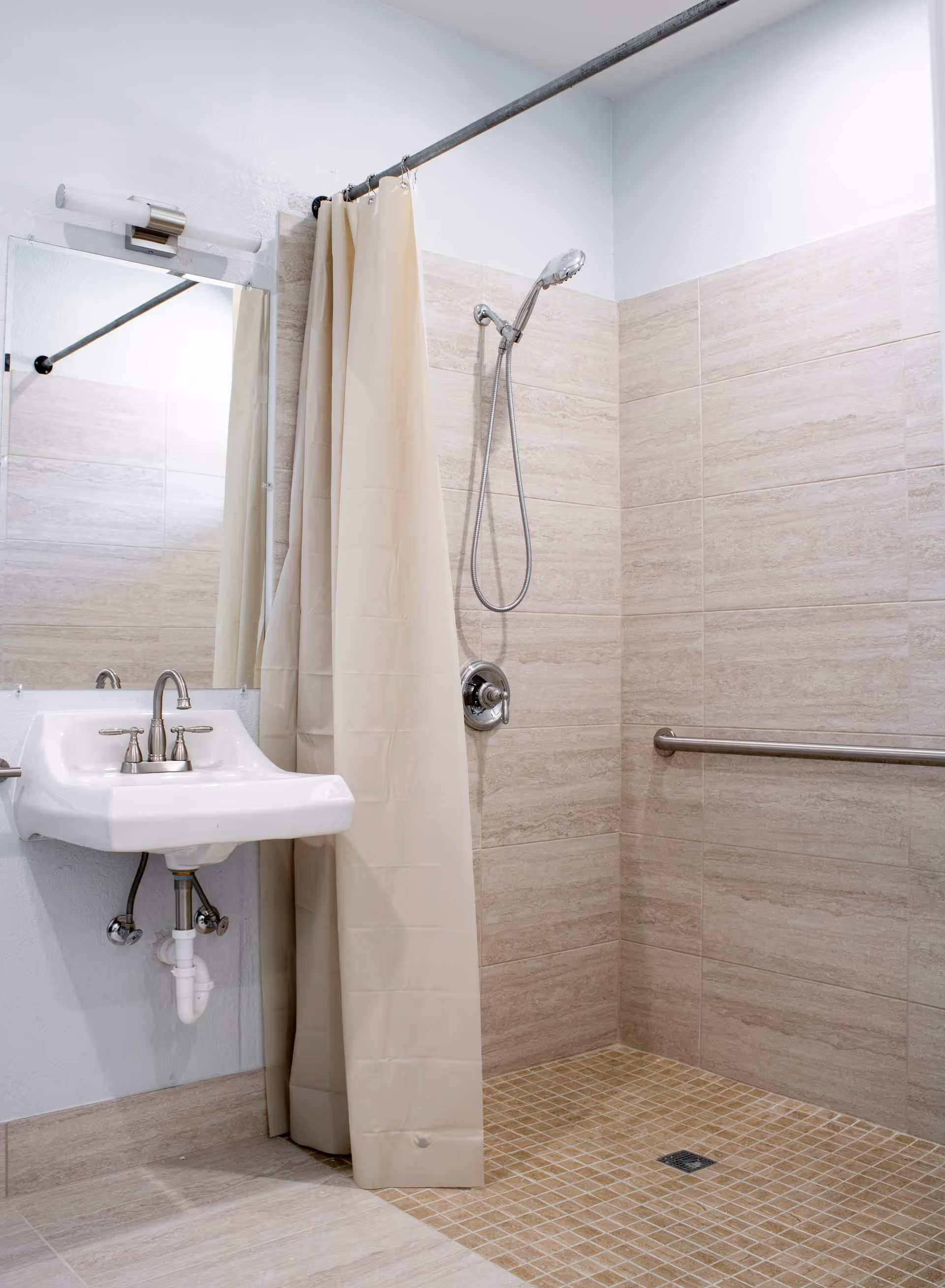 Accessible bathroom with a wall-mounted sink, shower curtain, handheld showerhead and grab bar.