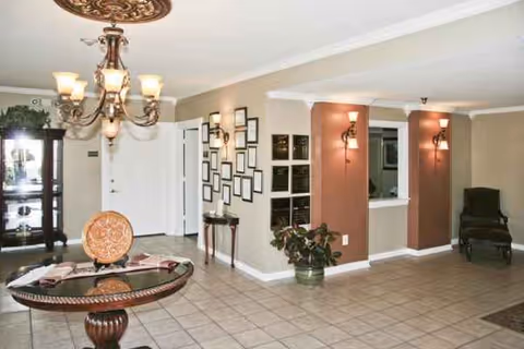 Senior living lobby with chandelier, reception desk, plants, seating, and framed wall art.