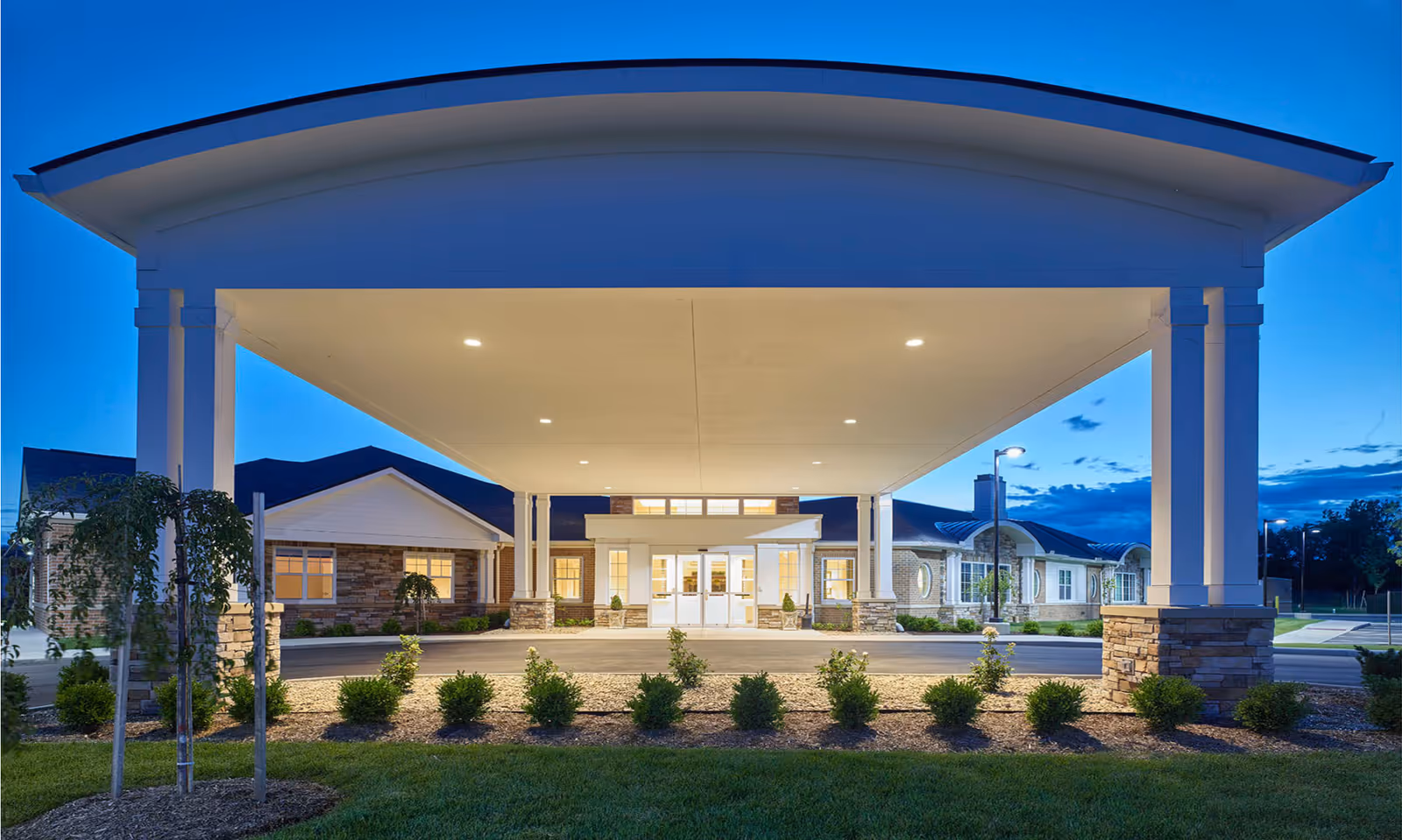 Front entrance of Kauhale Centerville with a large covered porte-cochere, lit entryway and landscaped driveway at dusk.