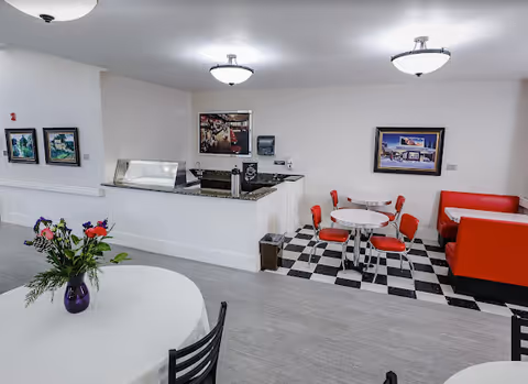 Retro-style dining area with red booths and chairs, round tables, a serving counter and framed artwork on the walls.