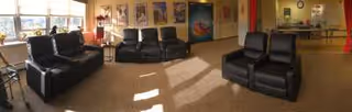 Sunny common lounge with several black reclining chairs, large windows, and artwork on the walls.