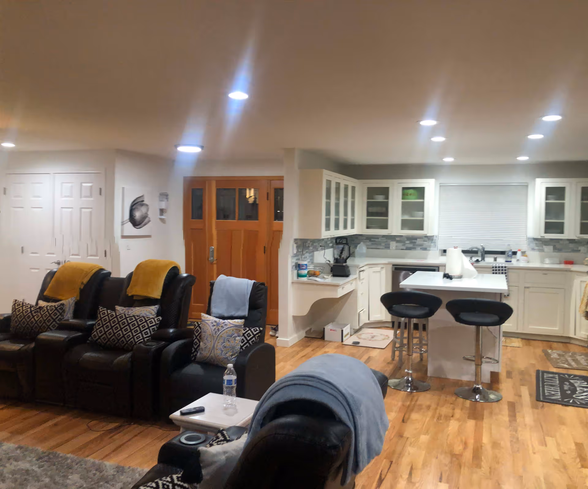 Open-plan living room and kitchen with several recliner chairs facing a coffee table and a kitchen island with stools on hardwood floors.